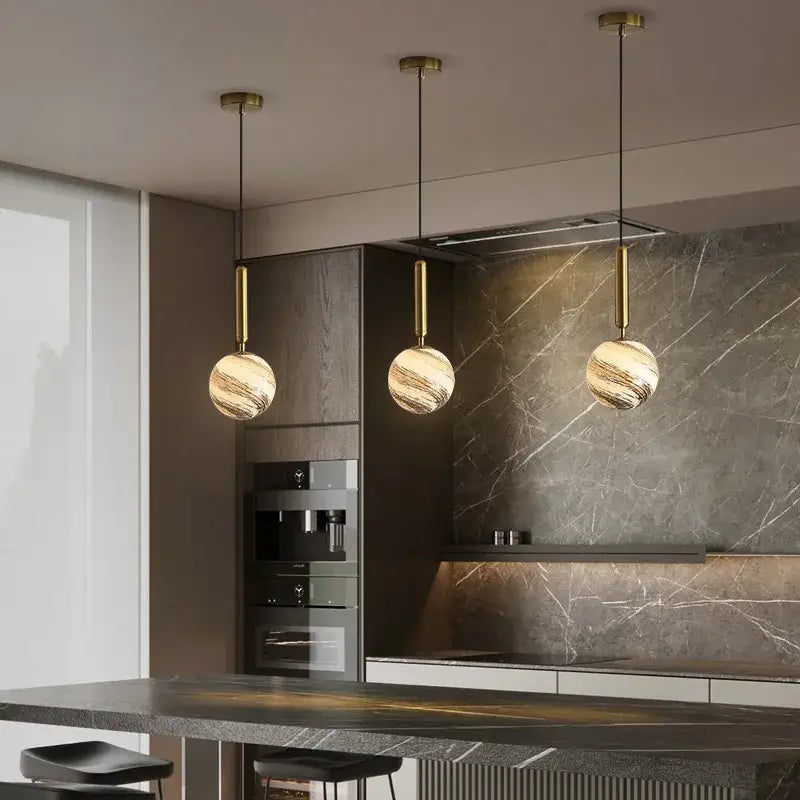 Three elegant cream and blue glass planet pendant lights with marbled spherical shades and brass rods for bedroom use