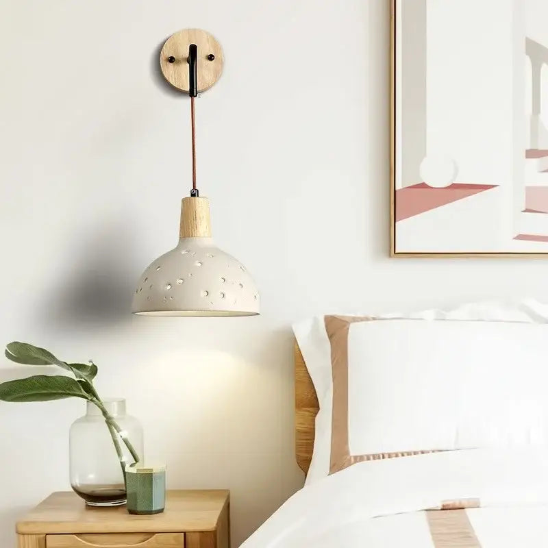 Modern cream ceramic wall lamp with circular perforations and pull chain switch suspended by wood and black metal