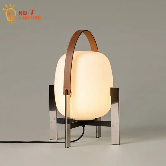 Modern cream designer metal glass table lamp with frosted body, sleek legs, and brown leather handle for bedroom decorbites