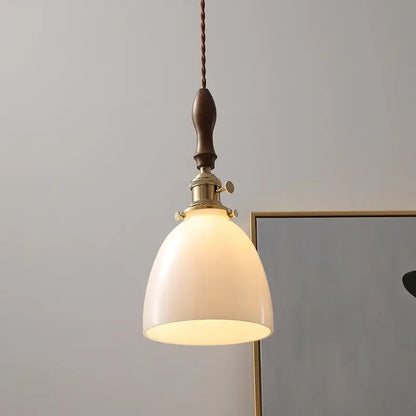 A warm-toned modern cream glass copper led pendant light with brass fixture and dark wood handle for dining room