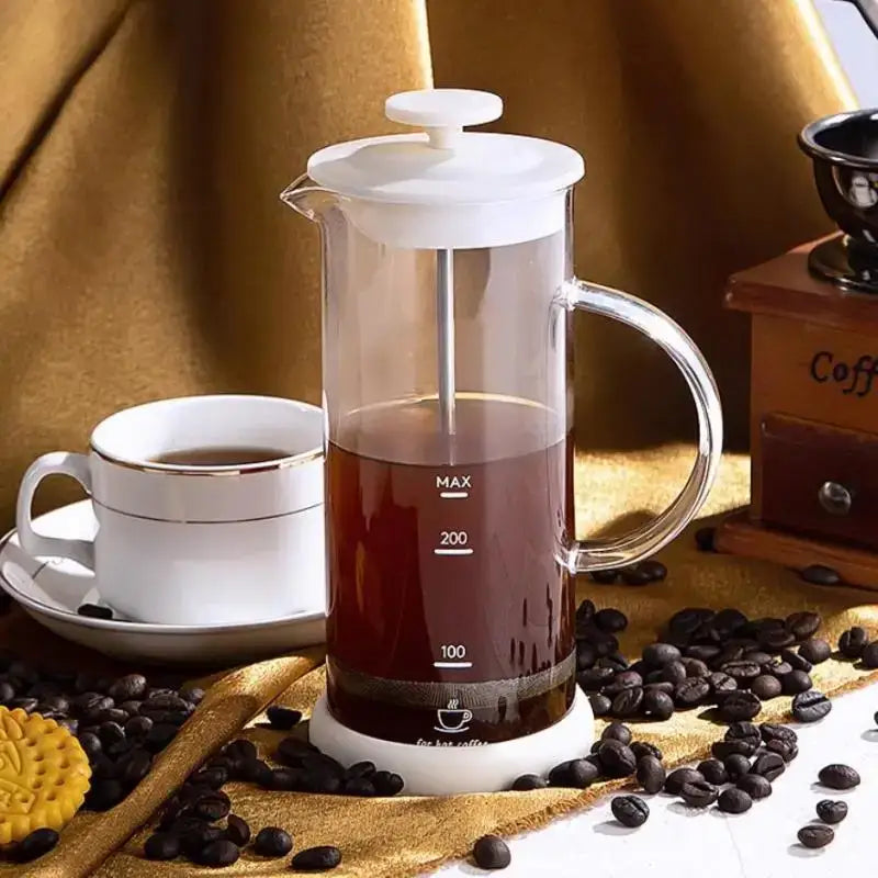 Modern cream glass french press coffee maker with white plastic lid and handle filled with dark coffee for hand foam mixer use