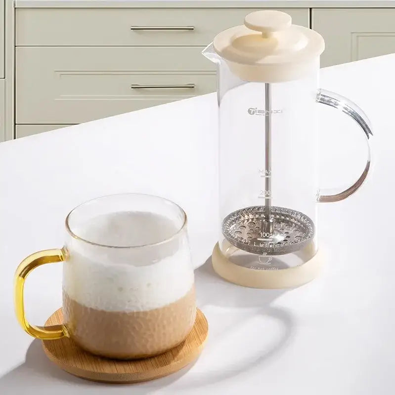 Modern cream glass french press coffee maker with a stainless steel plunger and hand foam mixer blender features