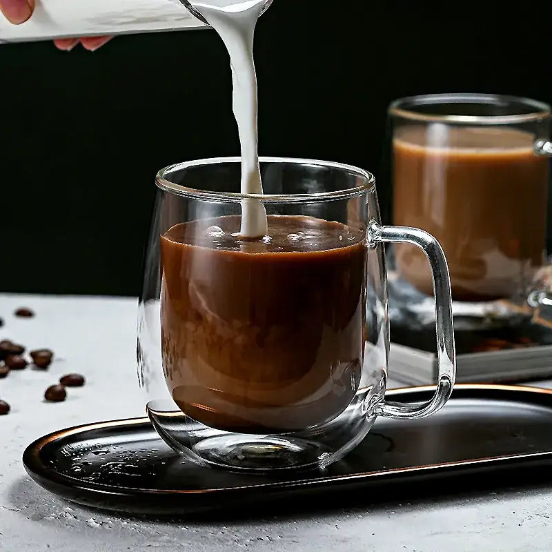 Modern double walled glass coffee mug with a sturdy handle filled with espresso being poured from a white pitcher for decorbites glass coffee use