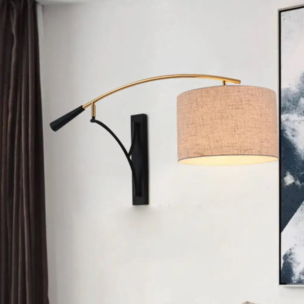Modern drum shade wall lamp in flaxen coffee with a curved gold metal arm and beige textured fabric shade for bedroom