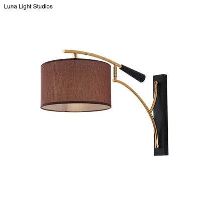 Modern drum shade wall lamp with a flaxen coffee textured fabric shade and curved gold-toned metal arm for bedroom use