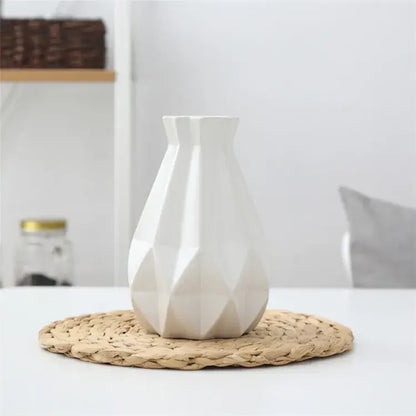 A sleek white decorbites ceramic diamond vase with geometric faceted design on a woven mat for living room decor