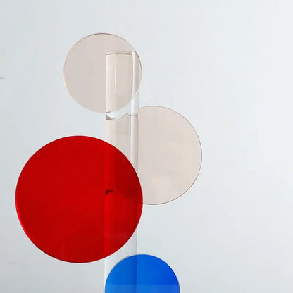A modern geometric crystal circle sculpture with red blue and beige discs on clear rods for home decor