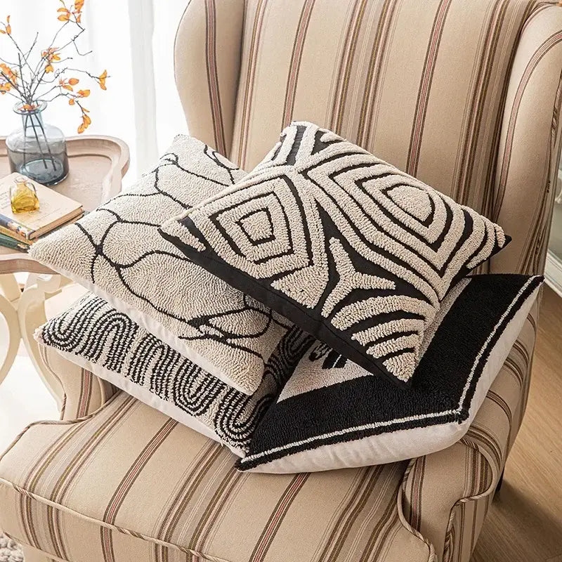Three black and cream decorbites geometric embroidered cushion covers with textured patterns on a striped armchair