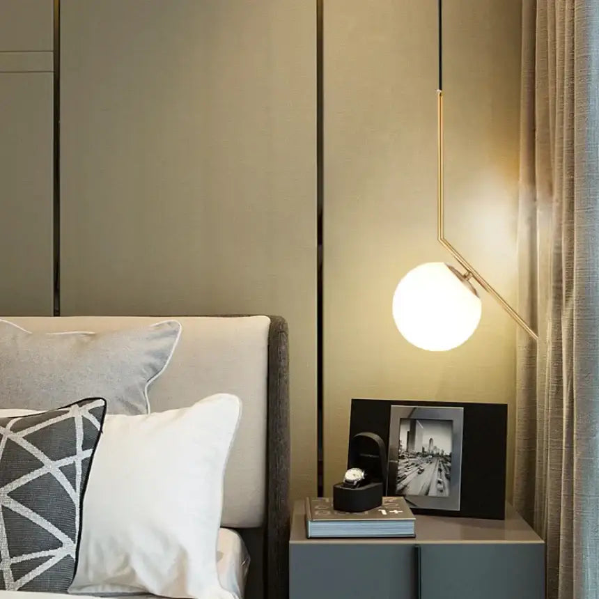 A modern minimalist glass pendant light with frosted spherical bulb and gold arms for bedroom bedside chandeliers
