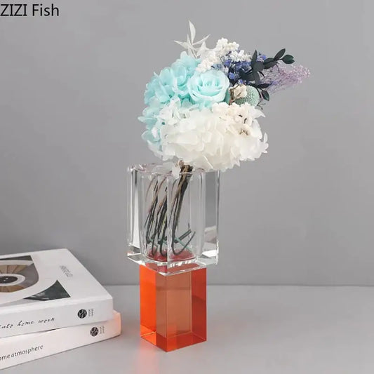 Clear acrylic geometric square vase with vibrant orange base holding artificial flowers in blue white and purple hues decorbites geometric square decor