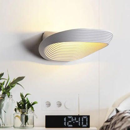 Modern white wall light with sleek curved design and concentric ridges producing warm white light for bedrooms