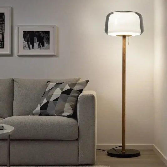 Modern glass floor lamp with a sleek white glass shade and wooden pole on a dark base for living room use