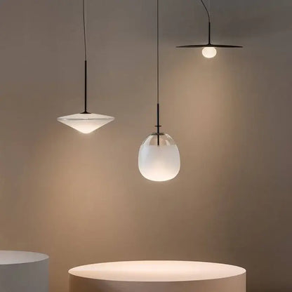 Three minimalist glass flying saucer chandelier pendant lights with frosted glass shades and black metal fixtures hanging