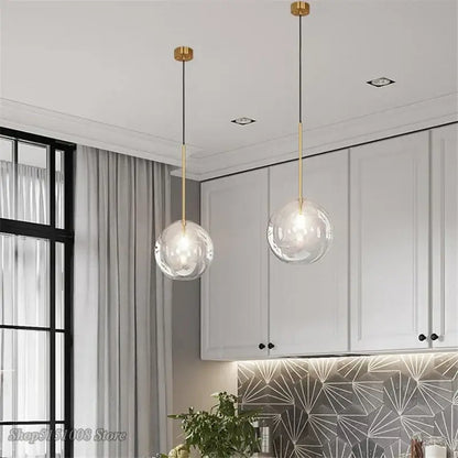 Two modern glass globe chrome pendant lights with gold fixtures and black cords hang in a dining room setting