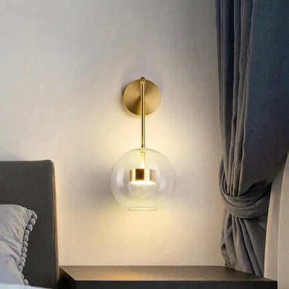 Modern gold wall lamp with adjustable direction featuring a spherical glass shade for minimalist bedroom lighting decorbites