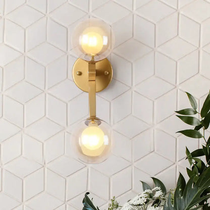 Modern gold amber glass wall light fixture with two spherical shades emitting warm glow for bedroom accent