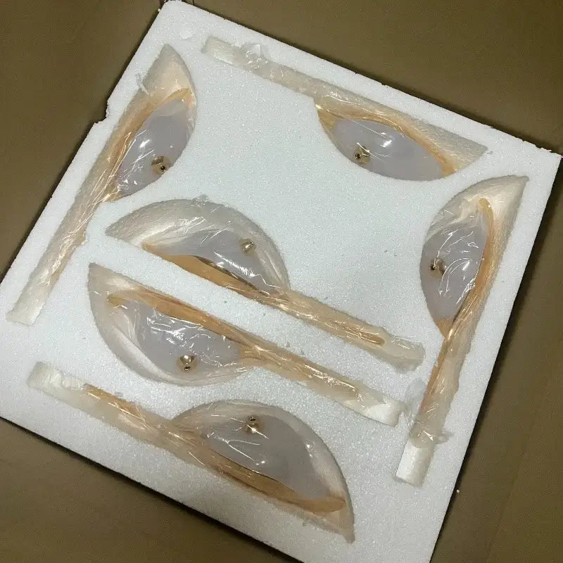 Five translucent beige silicone bra cups with gold hardware displayed in white foam unrelated to pendant light iron finish