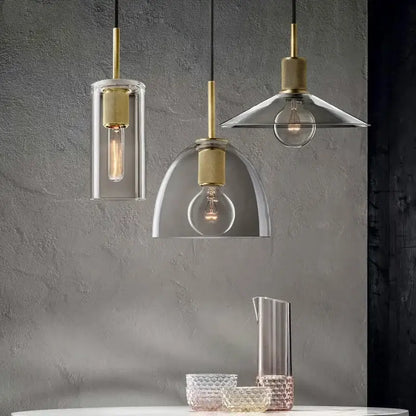 Three modern gold and clear glass led pendant lights with brass accents and geometric shades above dining table