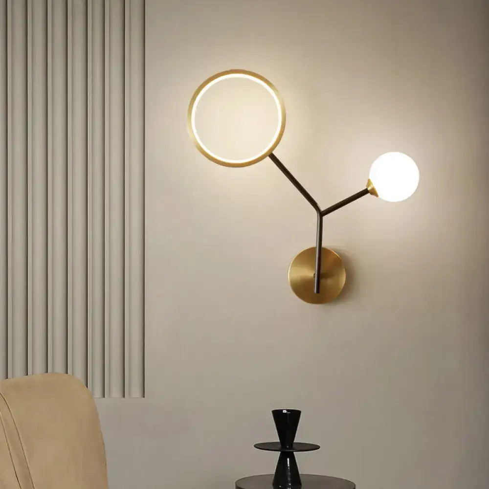 Modern gold and cream glass wall sconce lamp with circular ring light and spherical bulb on sleek brass base for bedroom lighting