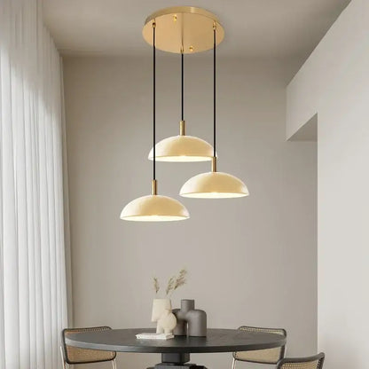 Modern pendant light with cream dome shades and gold-toned fixtures suspended by black cords for kitchen dining room