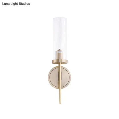 Modern brass-finished wall lamp with clear cylindrical fluted glass shade for bedroom sconce lighting