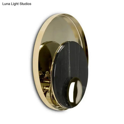 Gold-toned circular wall sconce with a black marble-like center and polished metallic finish.
