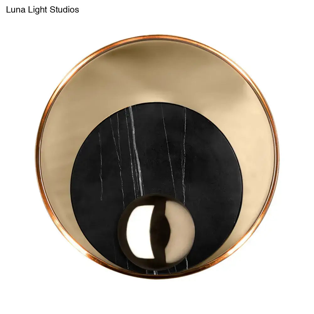 Modern gold and black marble wall sconce with peacock tail feather design featuring polished gold ring and reflective sphere