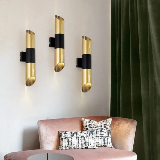 Three modern gold and black rotatable cylinder wall sconces with sleek curved design for bedroom lighting