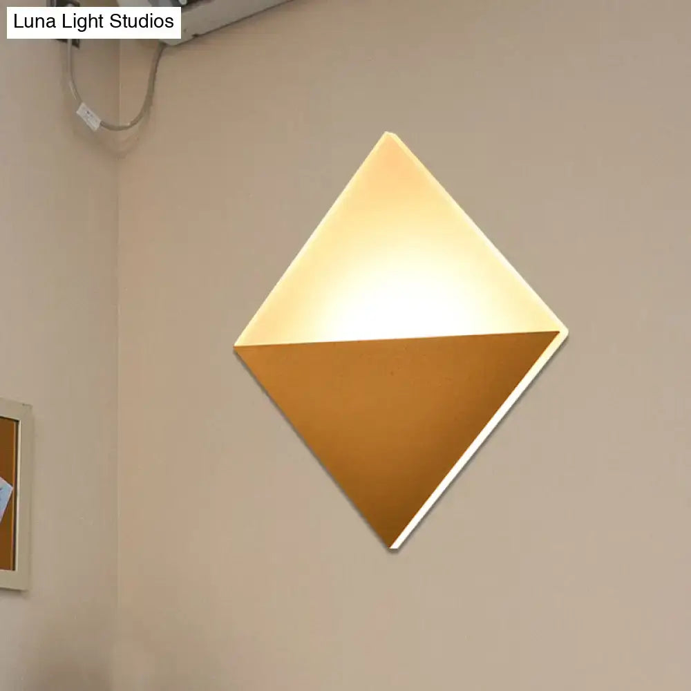 Modern gold and black wall sconce with diamond shape, warm glowing upper half, matte gold lower half, ideal for bedrooms