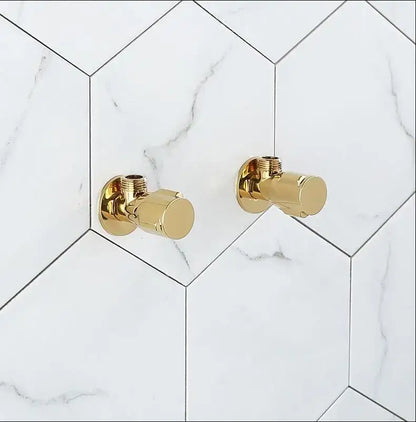 Two sleek decorbites brass triangle angle valves in gold finish mounted on white hexagonal marble tile wall