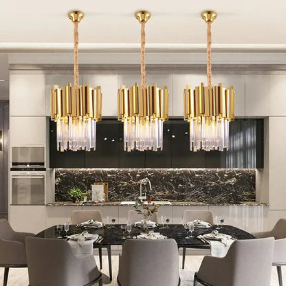 Three elegant gold and chrome decorbites crystal pendant chandeliers with cascading droplets above a dining table