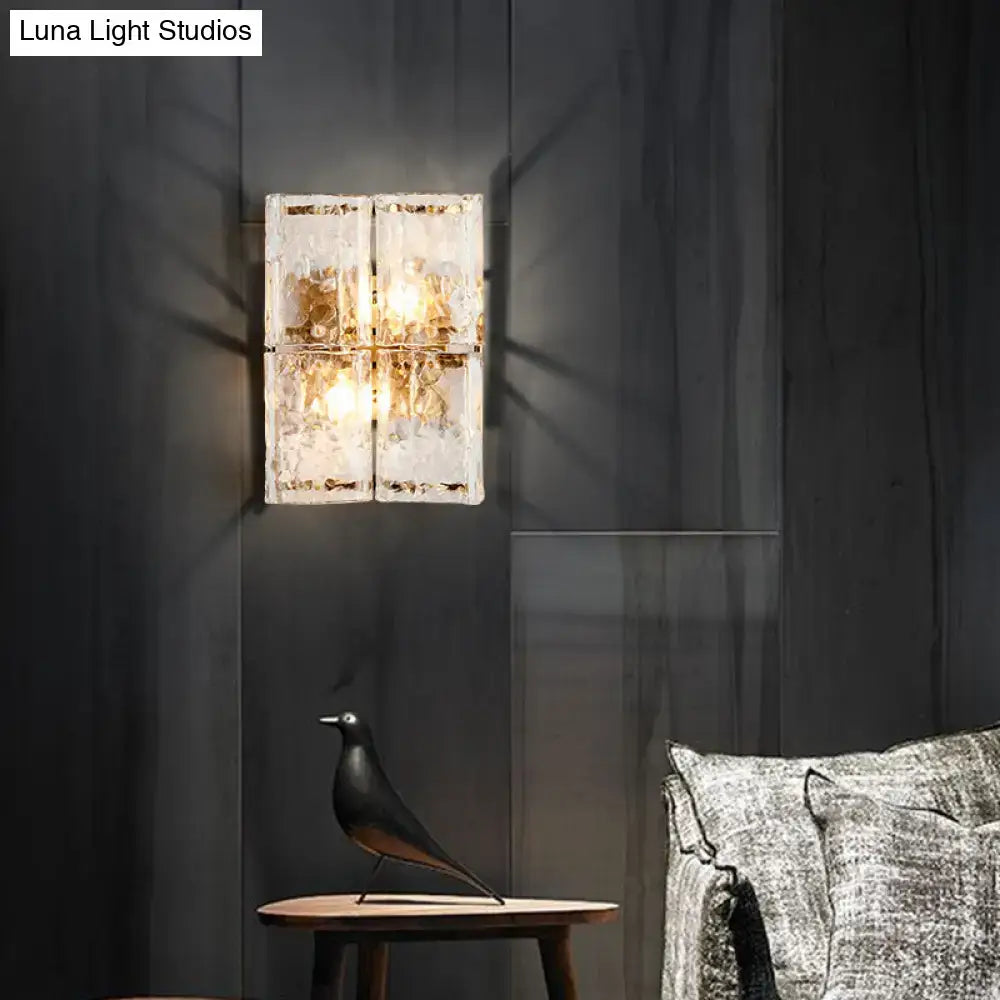 A modern gold two-light wall sconce with clear water glass shade and frosted panel for bedroom use