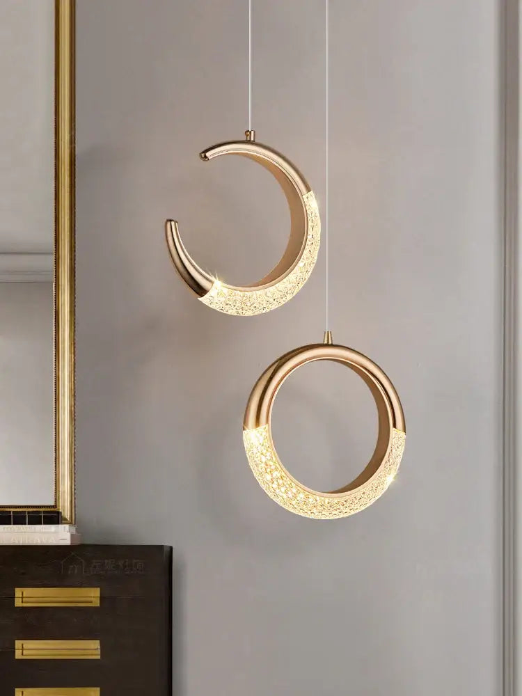 Two elegant gold-toned pendant lights with lace-like patterns and crescent design made of high-quality French metal for dining settings