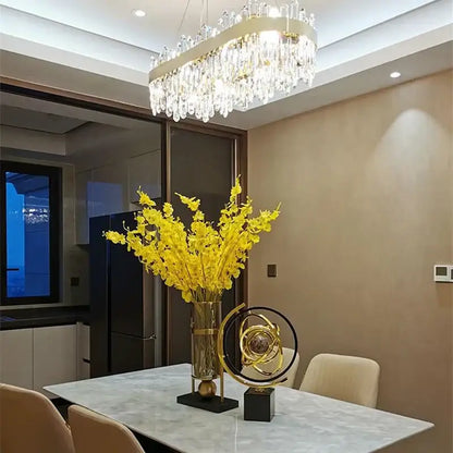 A tall glass vase with a gold metallic band and yellow flowers complements decorbites crystal circle ceiling chandelier decor