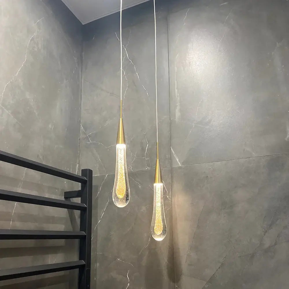 Two elegant gold-toned decorbites crystal glass led pendant lights with teardrop shades filled with golden glitter hang