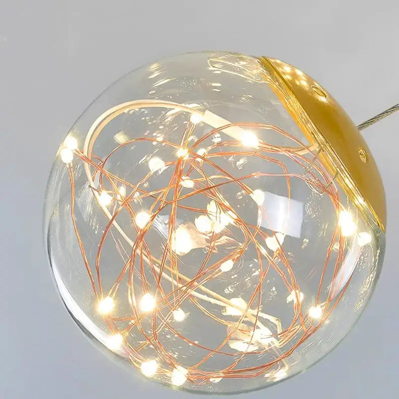 A clear glass globe pendant light with warm white led fairy lights and gold cap featuring a brushed stainless finish