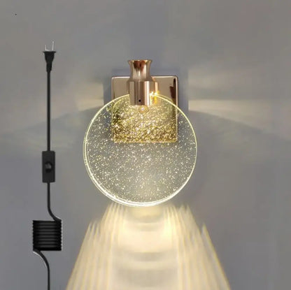 A modern gold crystal wall lamp with a circular glass globe filled with golden glitter and rose gold base for decorbites crystal wall decor