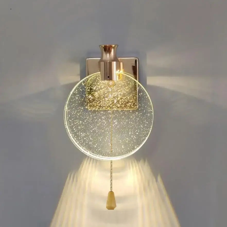 A modern wall lamp with a clear glass globe filled with golden glitter and a brushed brass decorbites crystal wall fixture