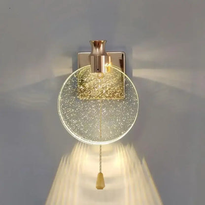 A modern wall lamp with a clear glass globe filled with golden glitter and a brushed brass decorbites crystal wall fixture