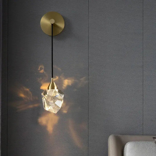 Modern gold crystal wall sconce light with a circular base and faceted crystal pendant casting warm light