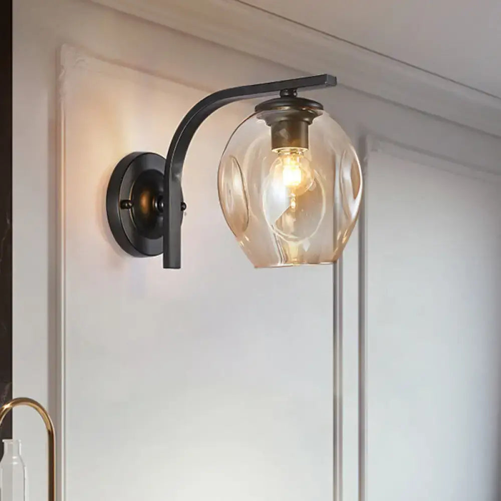 Modern gold curved arm glass wall sconce with black wrought iron and amber textured globe for bedroom lighting