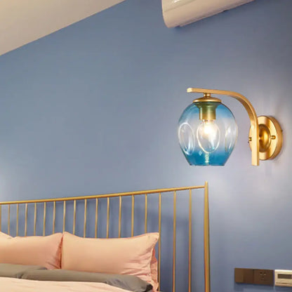 Modern gold curved arm glass wall sconce with blue gradient glass globe and gold-toned metal arm for bedroom light