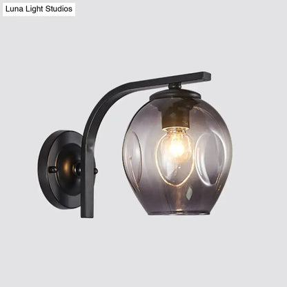 A sleek black metal wall sconce with curved arm and smoked glass globe featuring an exposed filament bulb
