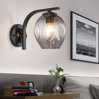 A sleek black metal wall sconce with a curved arm and translucent gray glass globe for bedroom lighting