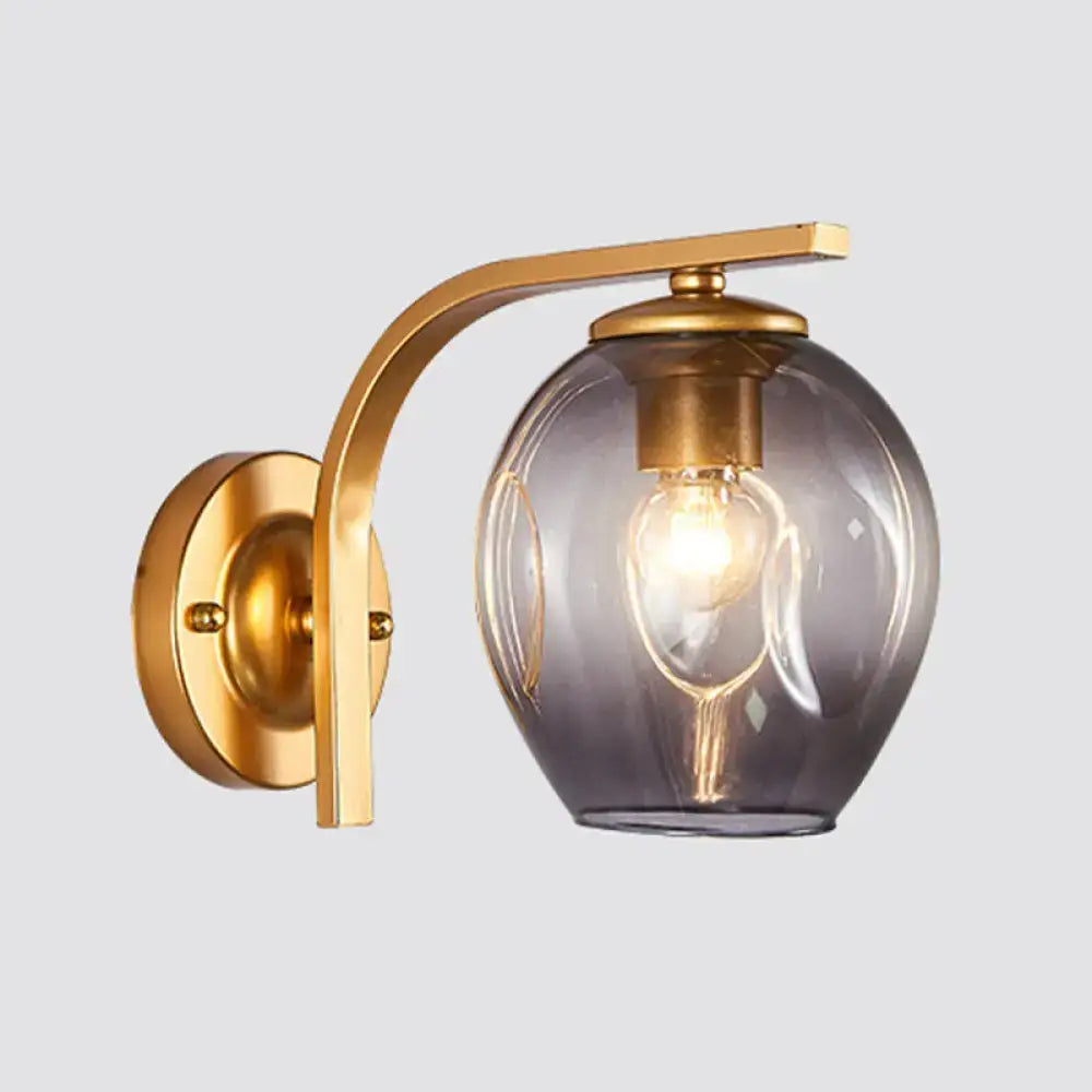 Modern gold curved arm glass wall sconce with brass finish and smoky globe for bedroom featuring exposed filament bulb