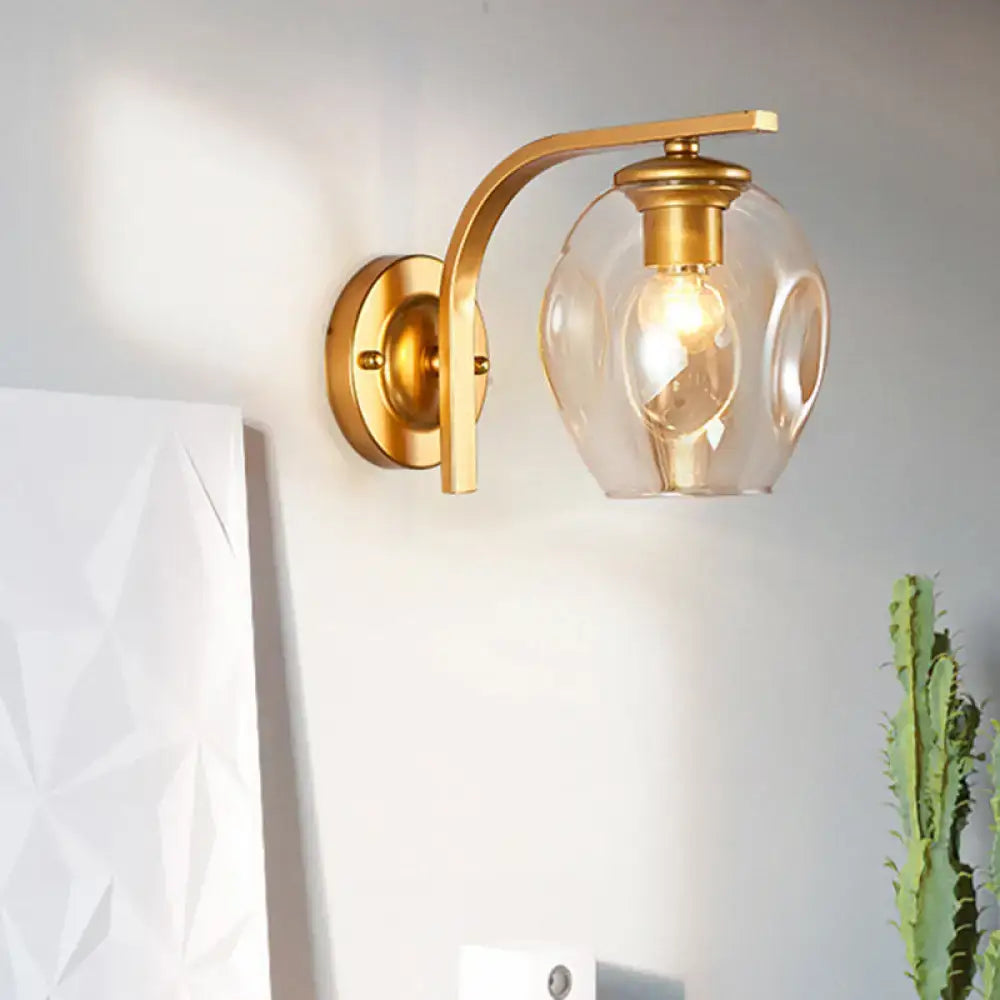 Modern gold curved arm glass wall sconce with clear rounded shade and exposed bulb for bedroom lighting in blue green decor