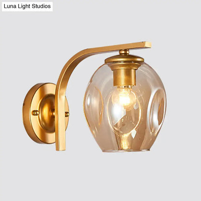 Modern gold curved arm glass wall sconce with textured amber globe and exposed bulb for bedroom lighting