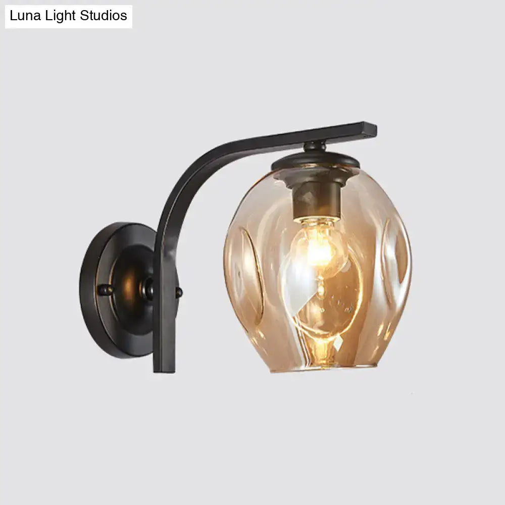 Modern gold curved arm glass wall sconce with amber textured globe and exposed bulb for bedroom lighting