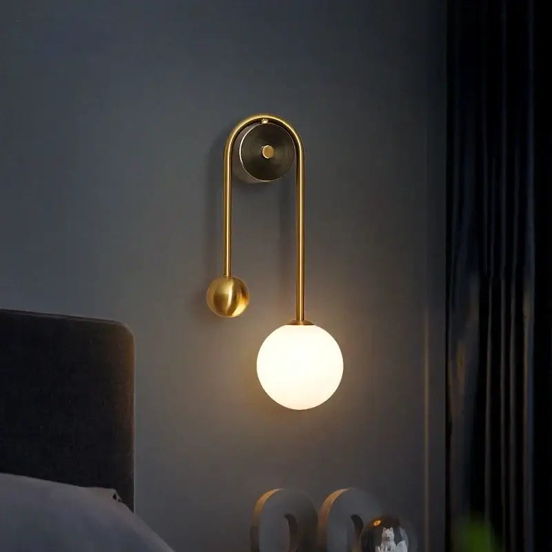 Modern gold decorbites glass ball led wall lamp with a gold-toned curved arm and spherical glass ball shade for bedroom use