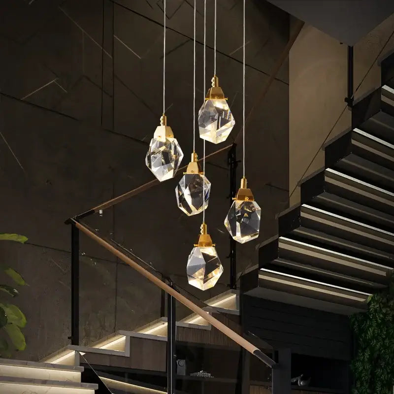 Five faceted diamond crystal chandelier pendant lights with gold fixtures hang above a modern staircase